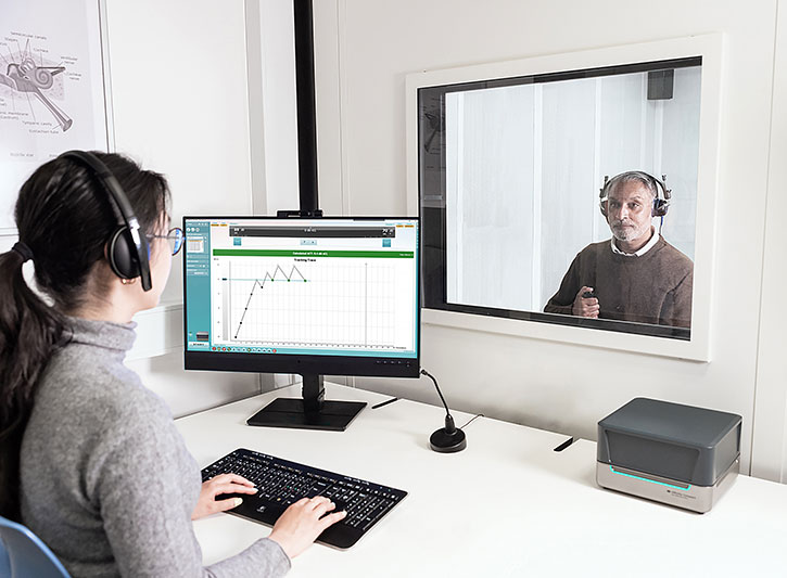 Der Pr&uuml;fer bedient die PC-Tastatur und den ACT-Testbildschirm in der Affinity Suite. Angeschlossen ist hier eine Affinity Compact. Im abgetrennten Raum tr&auml;gt der Kunde einen Kopfh&ouml;rer und best&auml;tigt w&auml;hrend des Tests mit der Antworttaste.