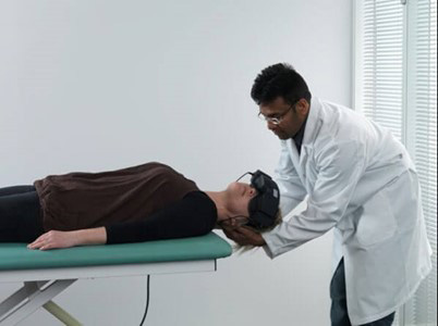 Clinician stood behind patient lying on their back on a green examination bed. The clinician is turning the patient's head toward the left at a 45-degree angle.