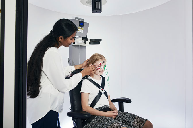 Young female patient sitting in Orion Auto-Traverse. Female clinician attaching electrodes to the patient's face.