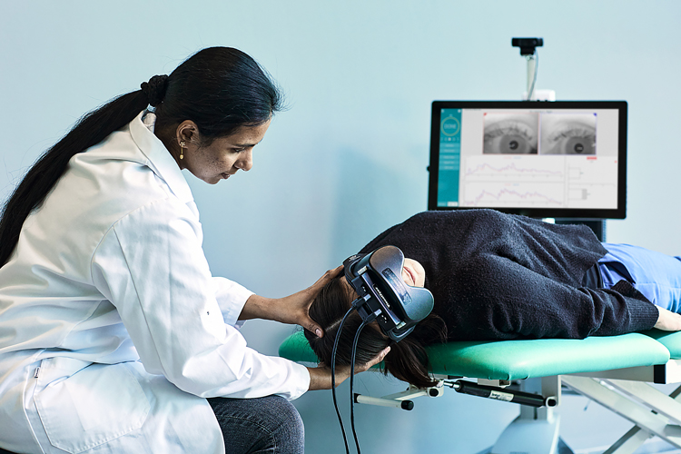 Clinician supporting the head and neck of a patient, who is laying supine on an examination bed with their head and neck hanging off the edge turned 45 degrees to their right.